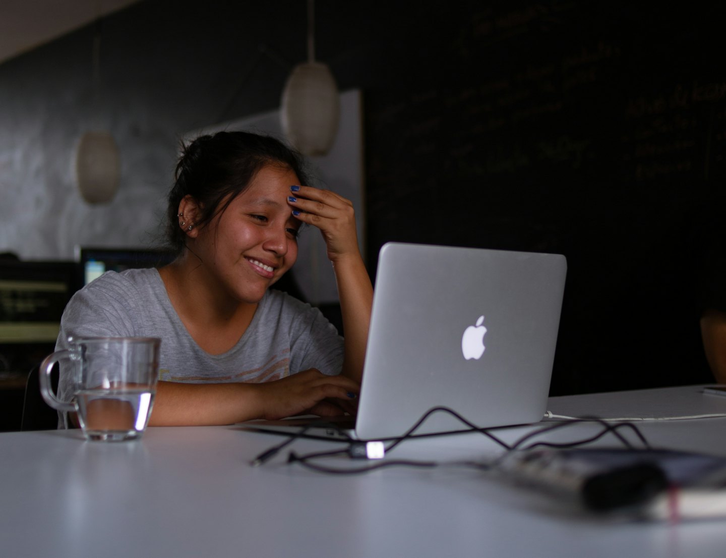 Giovane donna sorride al suo laptop argentato su una scrivania bianca.